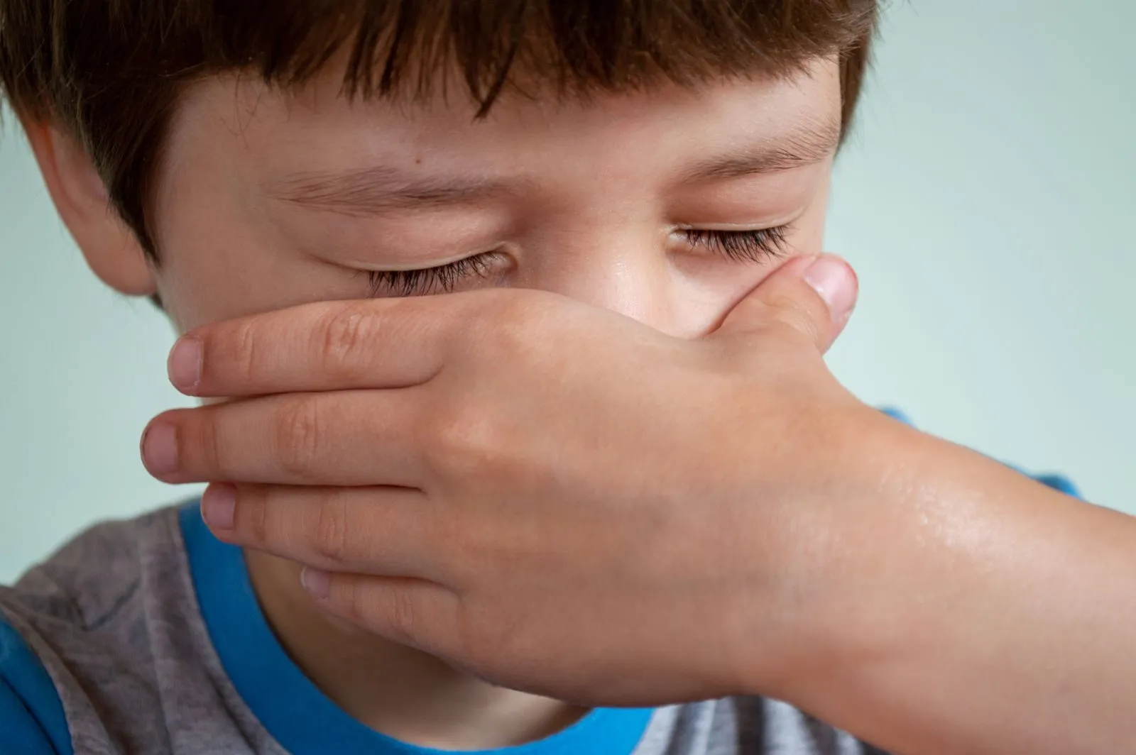 Jeune garçon, les yeux fermés, qui se frotte les yeux avec les mains