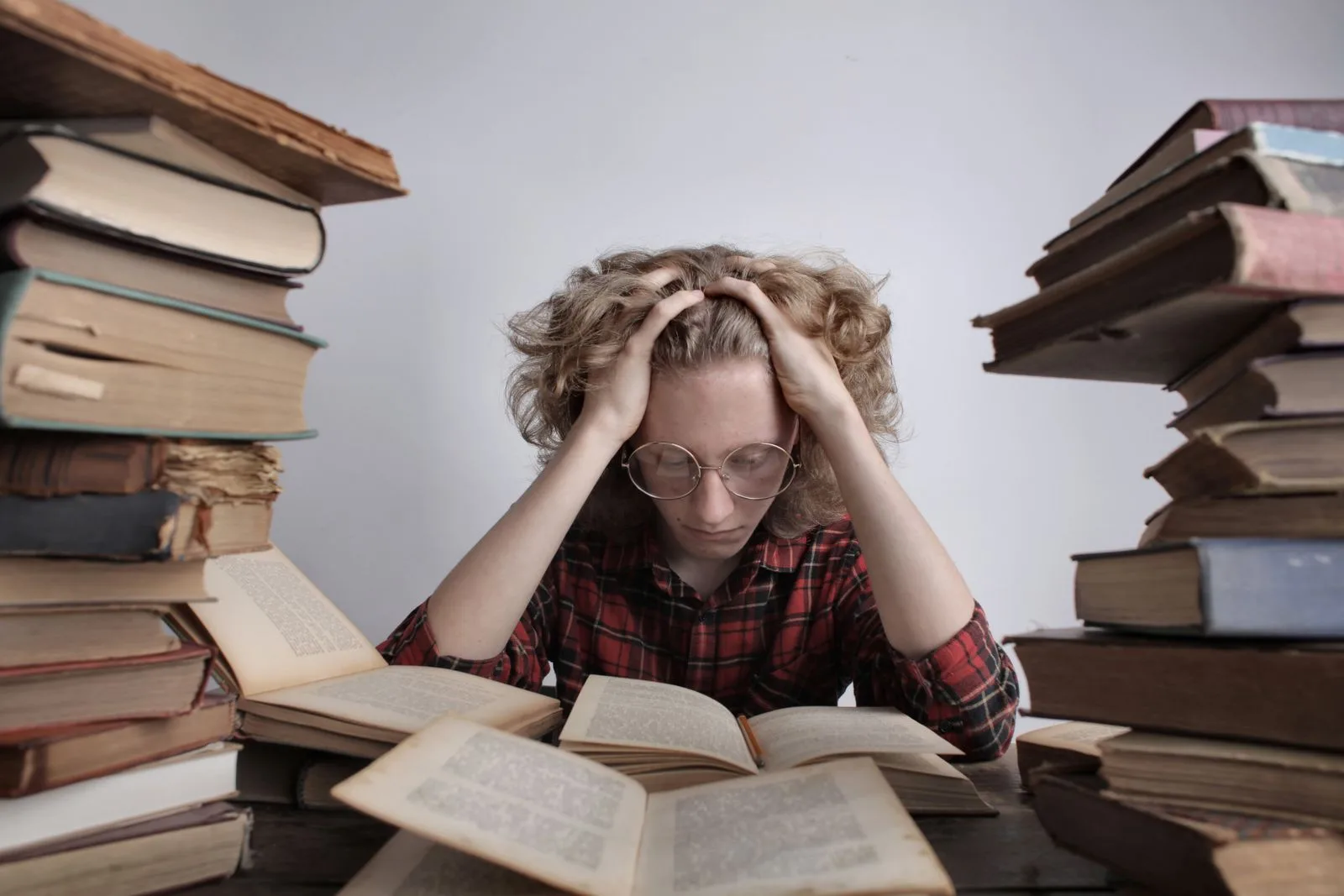 Adolescent fatigué à sa table de travail, entouré de livres, la main sur la tête